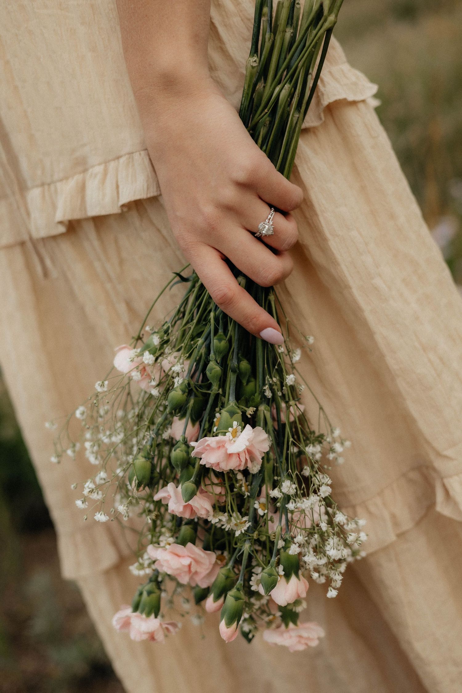 Close-up of hands holding delicate pink carnations and baby's breath bouquet against cream fabric.