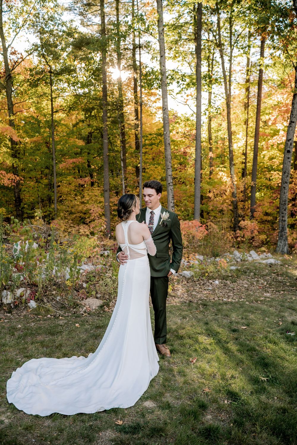 A couple shares an intimate moment in a wooded area with fall foliage during their wedding photoshoot.