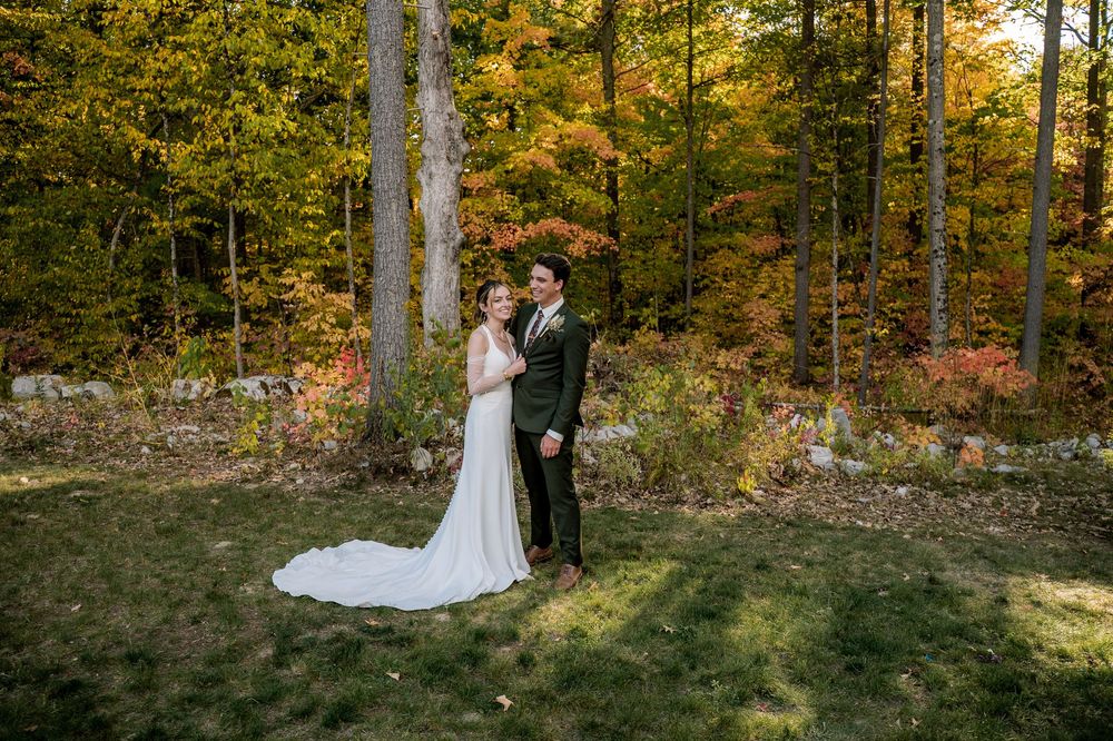 A couple shares a romantic moment in a sunlit autumn forest with golden leaves and tall trees in the background.