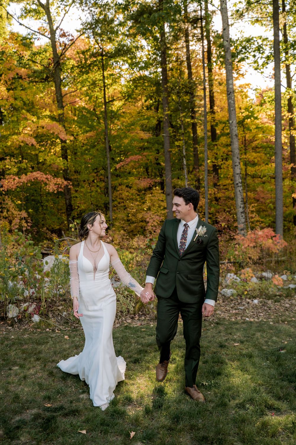 A couple walks hand in hand through a scenic autumn forest setting with golden foliage during a fall wedding.