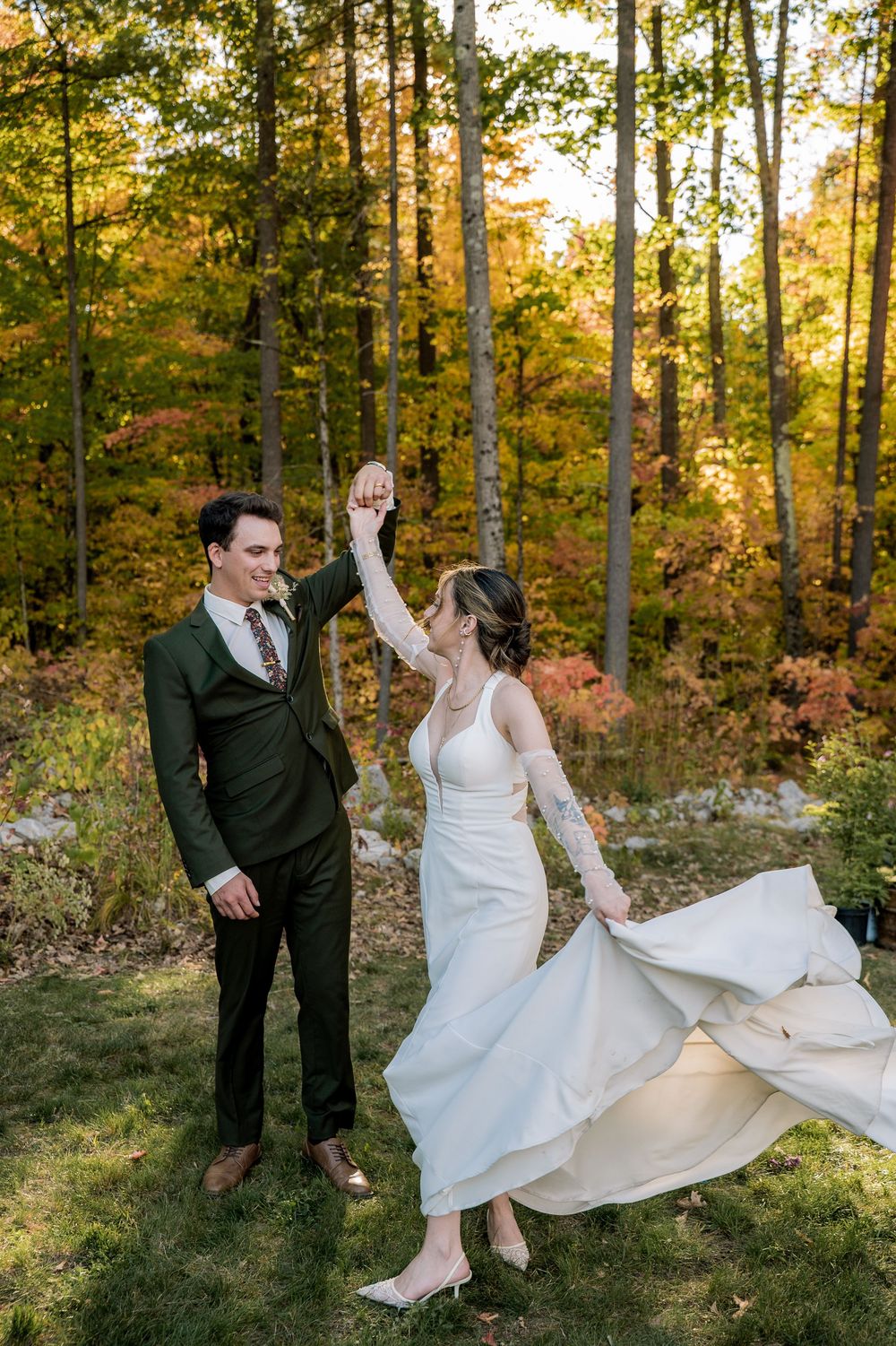 A playful wedding couple dancing and twirling in a wooded setting with autumn colors.