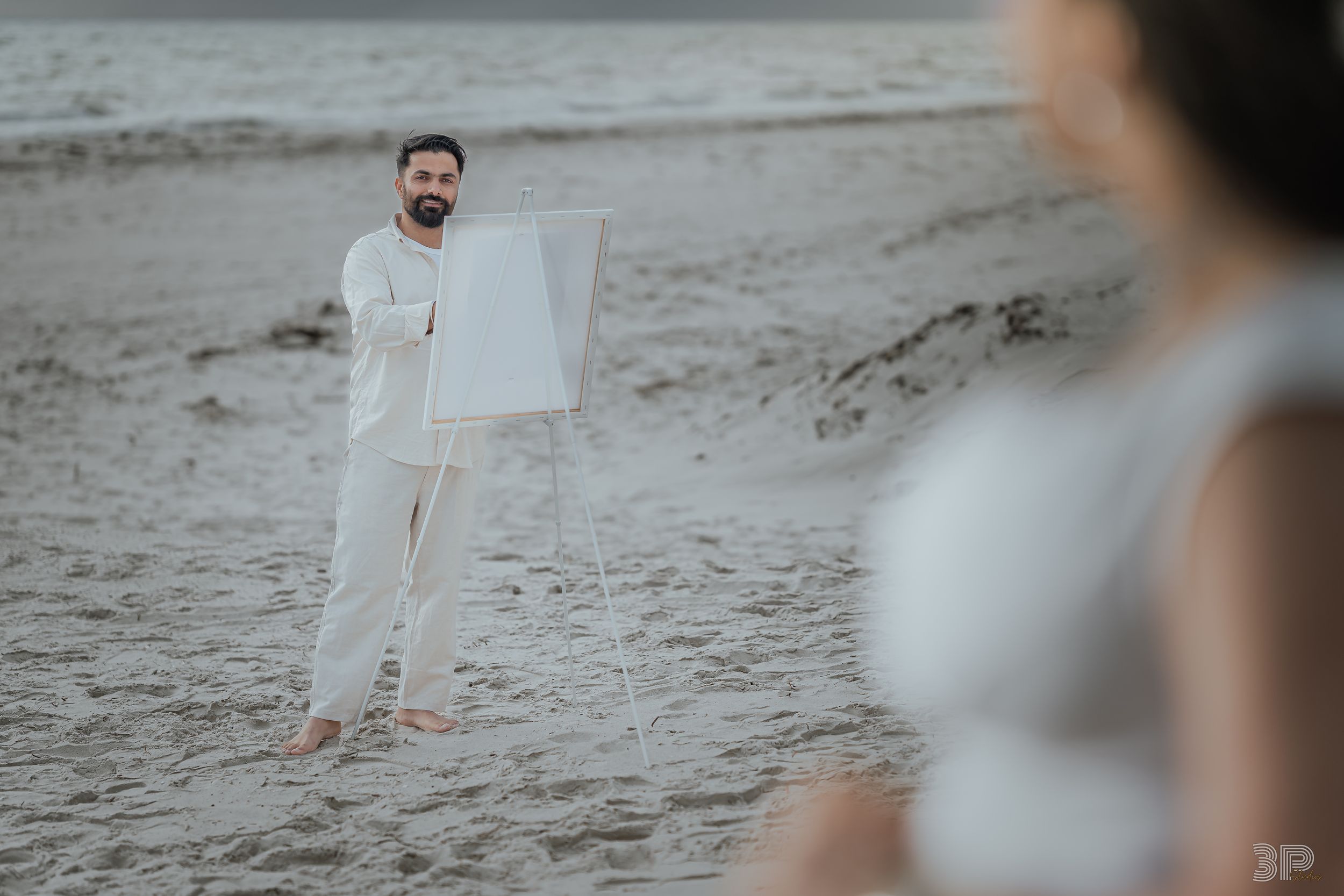 A couple shares a romantic moment on a sandy beach during a cloudy day.