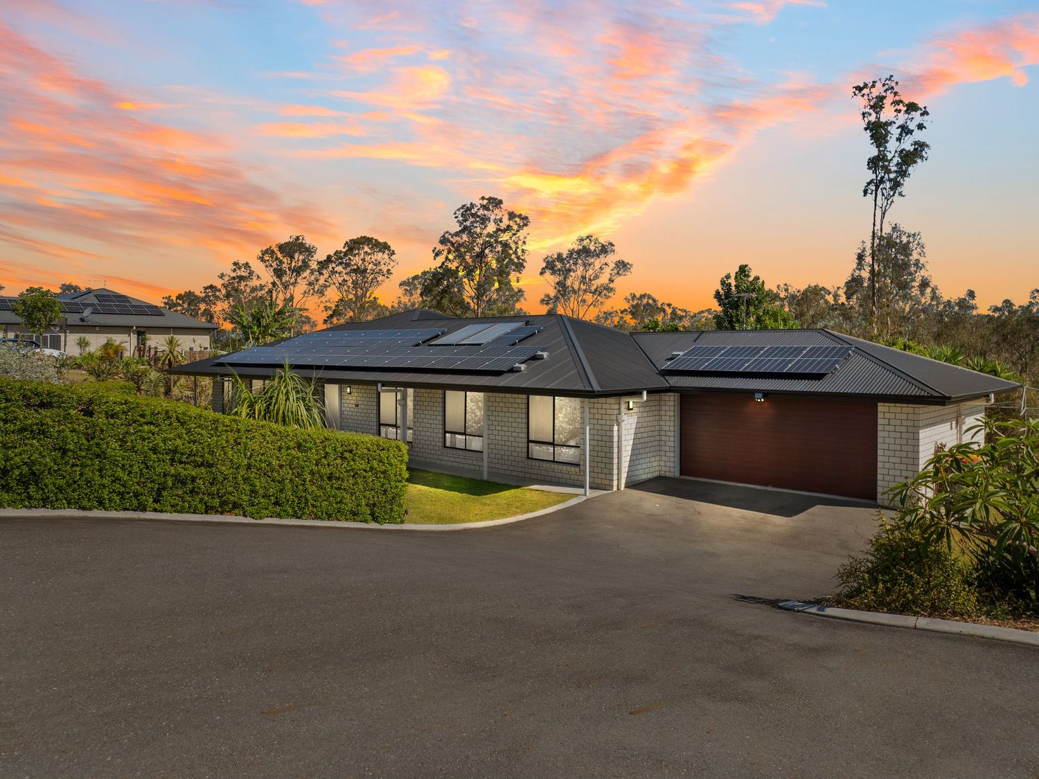 Residential street view at sunset with modern homes and pink-orange sky.