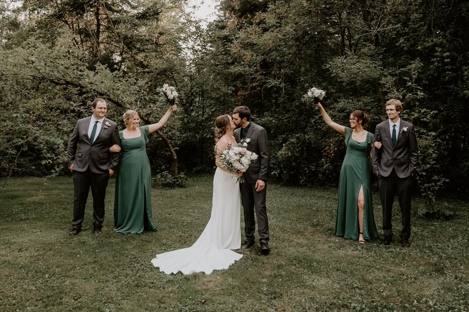 bride and groom in centre kissing with wedding party on either side holding up their bouquets