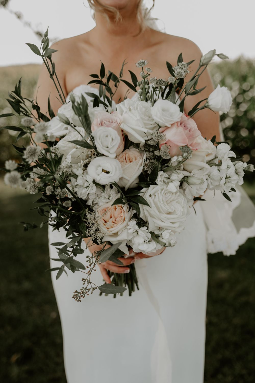 close up of bouquet of pink and and peach flowers surrounded by leafy greens