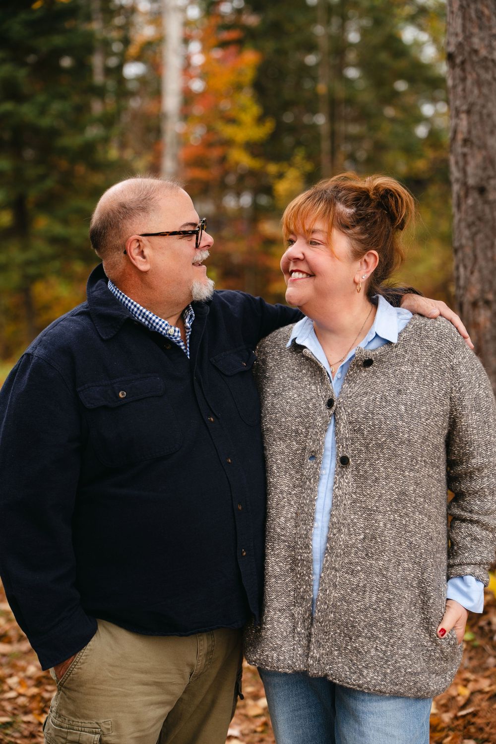 A couple shares a joyful moment together outdoors during autumn, wearing casual sweaters against a backdrop of fall foliage.