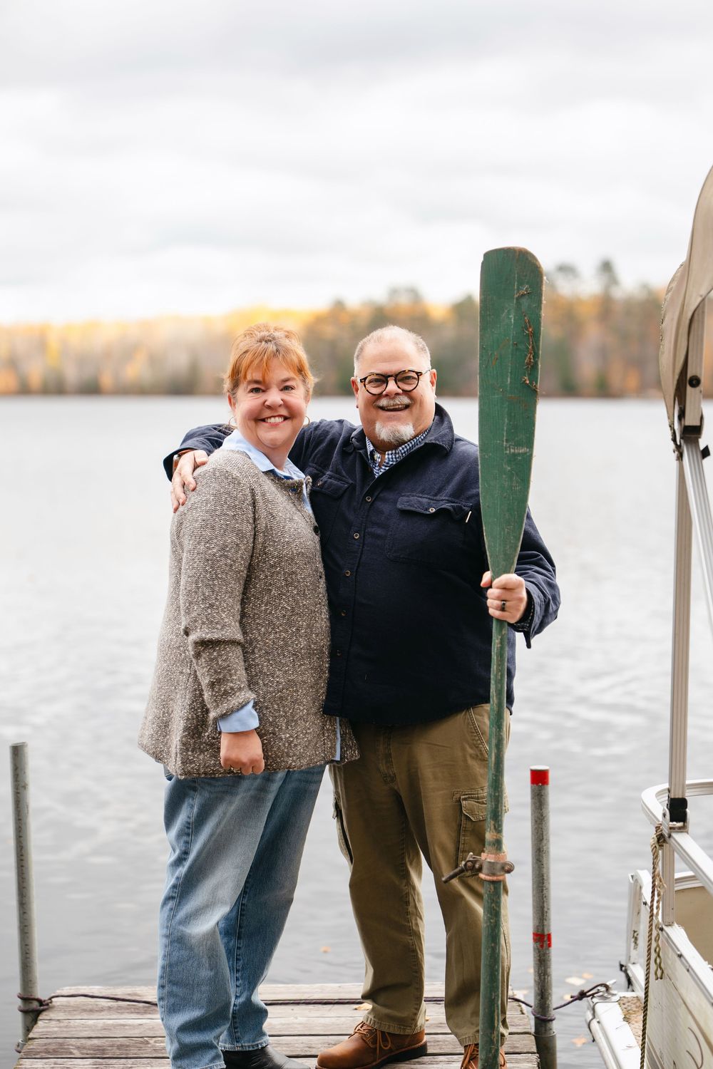 A couple shares a joyful moment together on a wooden dock by a lake during autumn.