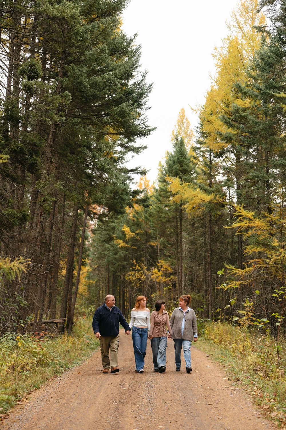 A group takes an autumn stroll down a dirt path through a forest with tall evergreen trees and golden foliage.