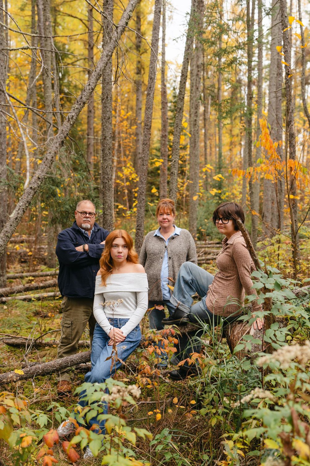 A group sits scattered among autumn foliage in a forest with golden yellow leaves and tall trees.