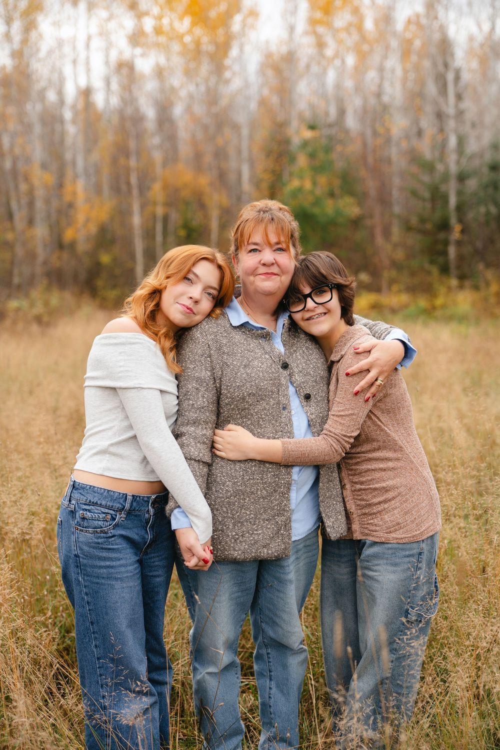Three people posing casually together in a field with autumn foliage and trees in background.