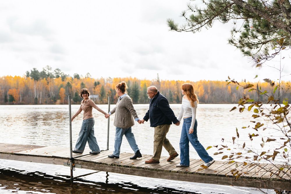 A group walks together on a wooden dock by a lake surrounded by autumn trees during golden hour.
