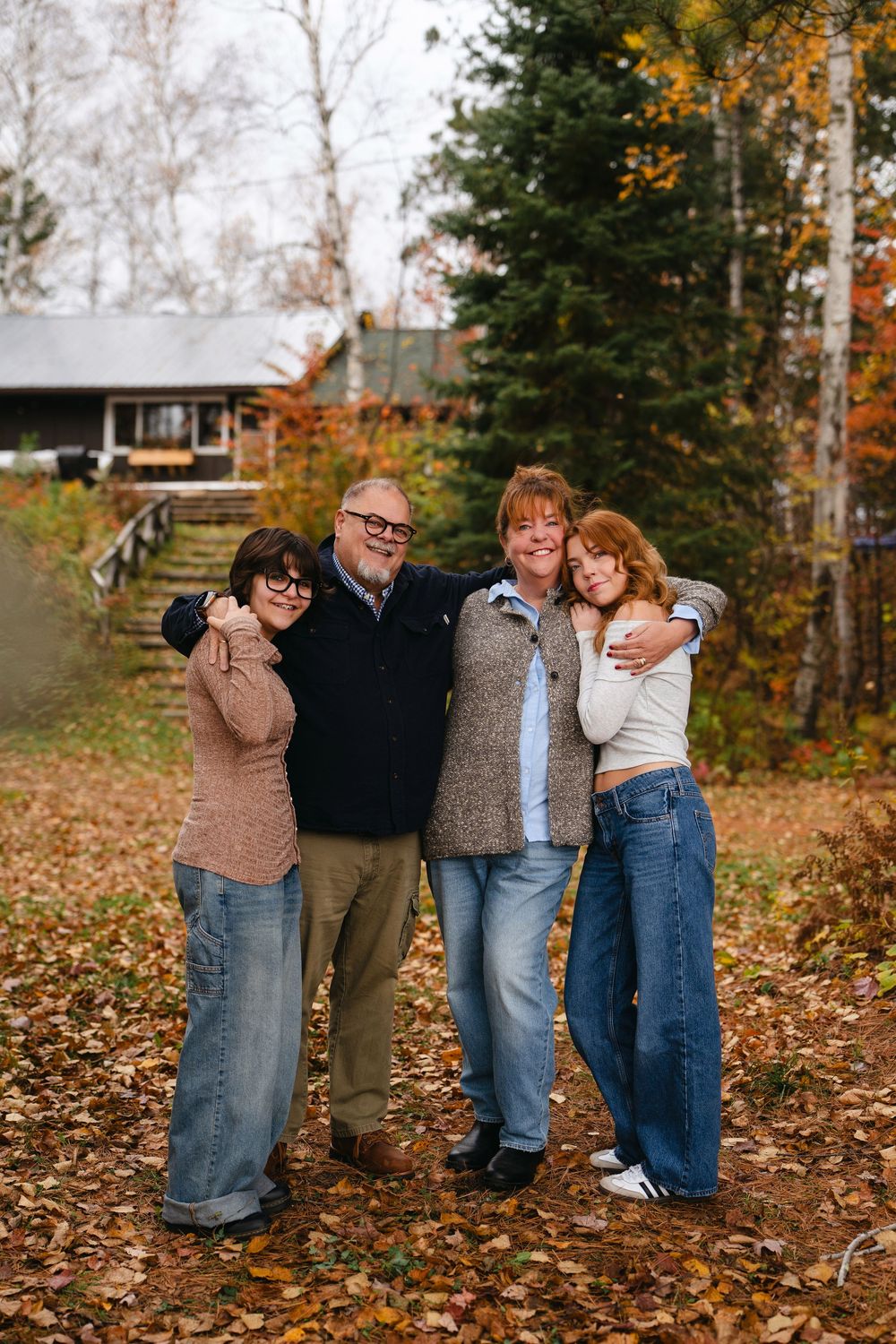 Family members pose playfully in fallen autumn leaves with trees and a cabin in the background.