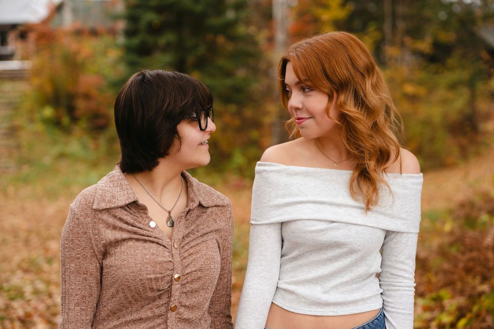 Two people share an intimate moment surrounded by autumn foliage in a romantic outdoor setting.