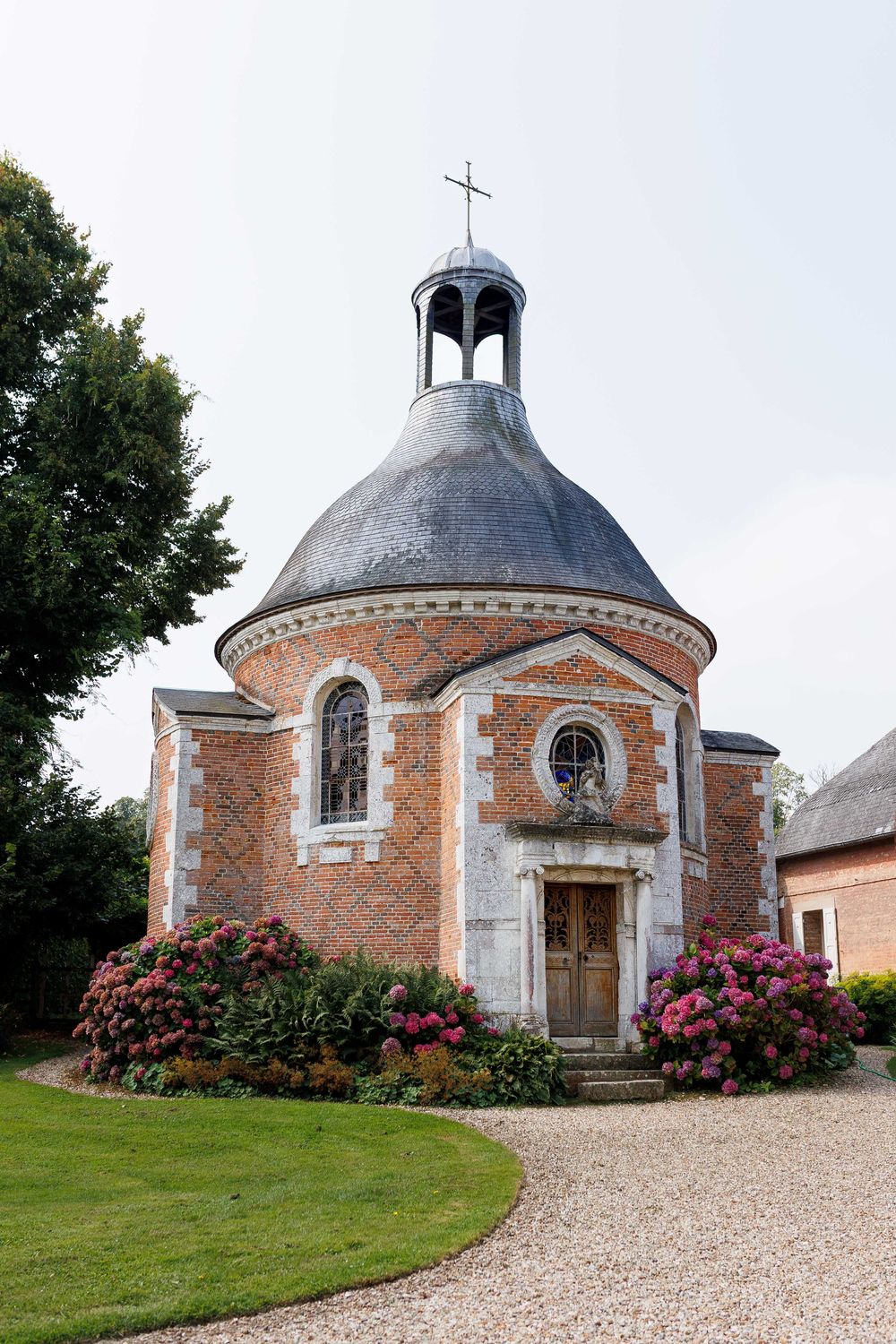 A historic octagonal brick chapel with a domed roof and pink flowering bushes shown from multiple angles on a gravel path.