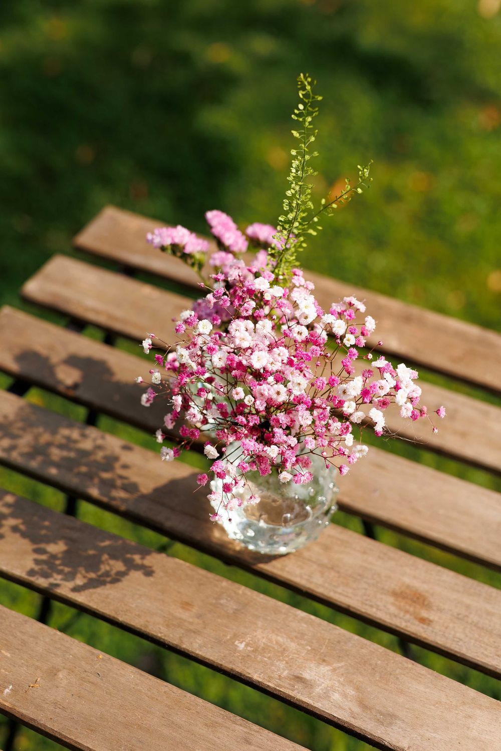 Pink baby's breath flowers arranged in a clear glass vase sitting on weathered wooden planks.