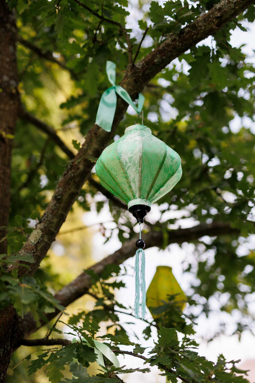 Glass butterfly ornaments in soft mint green hang from tree branches against a leafy backdrop.