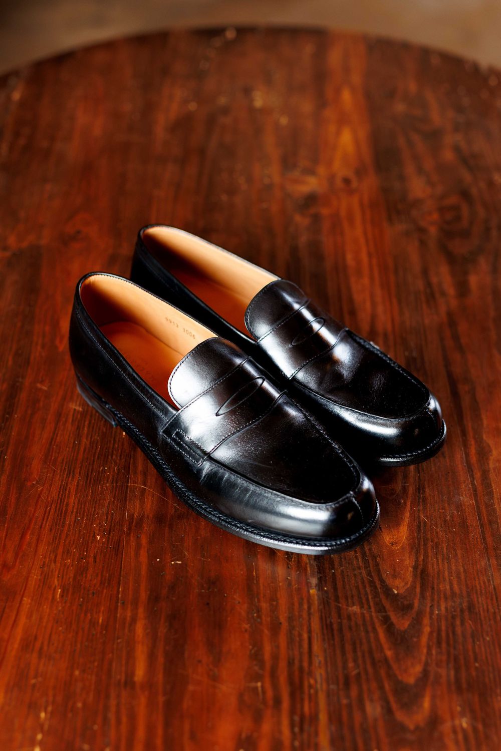 A pair of black leather penny loafers displayed on a polished wooden surface.