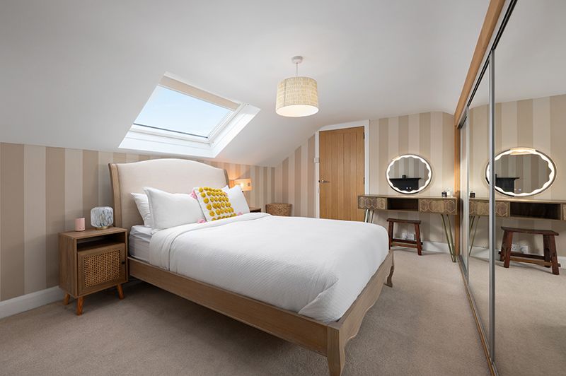 Modern minimalist bedroom with wooden accents, natural light from skylight, and clean white bedding.