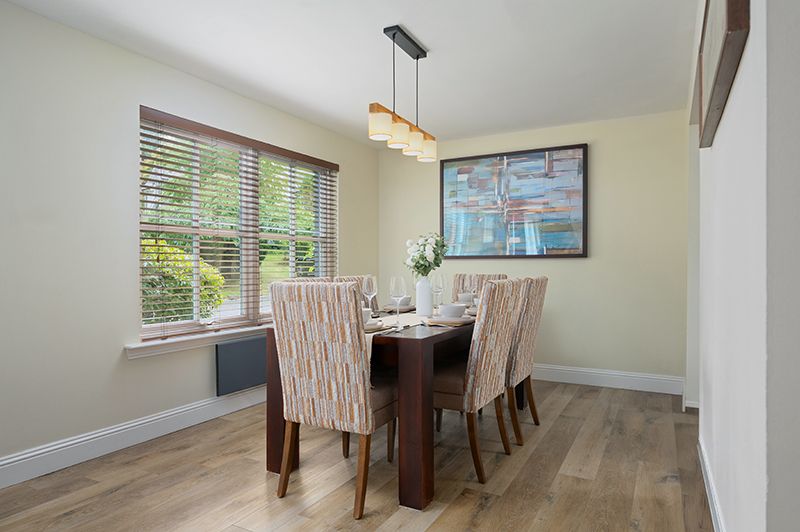 Modern dining room with wood table, upholstered chairs, window with blinds, and pendant lighting over table.