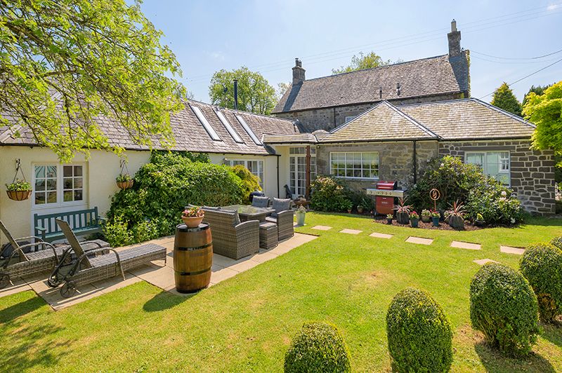 A panoramic view showing a stone cottage with well-maintained gardens and pathways in a rural setting.