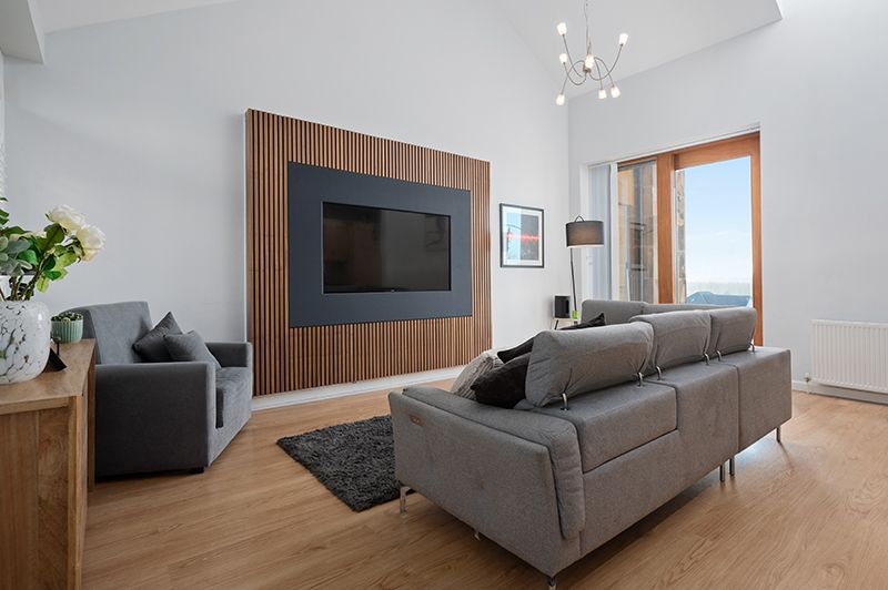 Modern living room with grey sectional sofa, wood paneled walls, and mounted TV in a minimalist interior design.