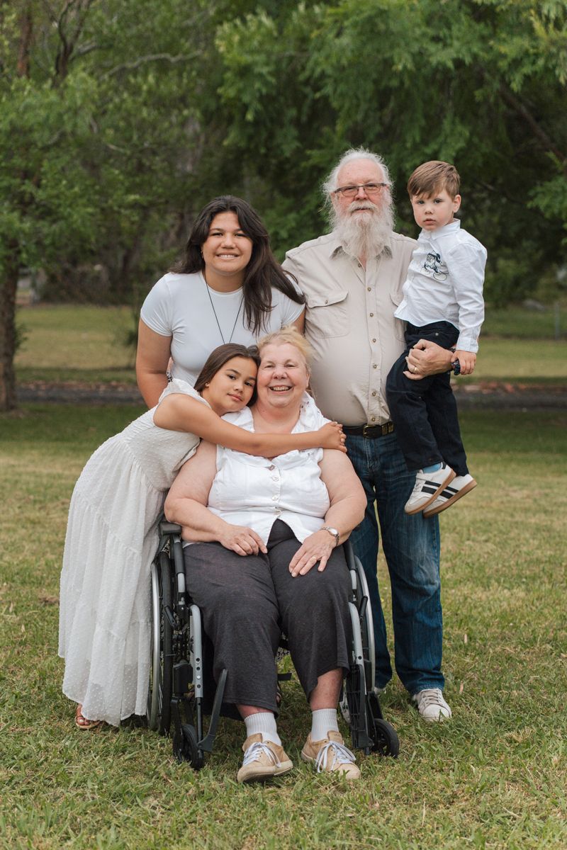 A family shares tender moments together outdoors while sitting on grass in a park setting in The Gables in Sydney Box hill