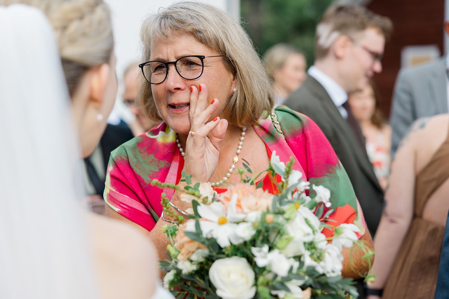 A group of people celebrate at an outdoor gathering with colorful flowers and joyful expressions.