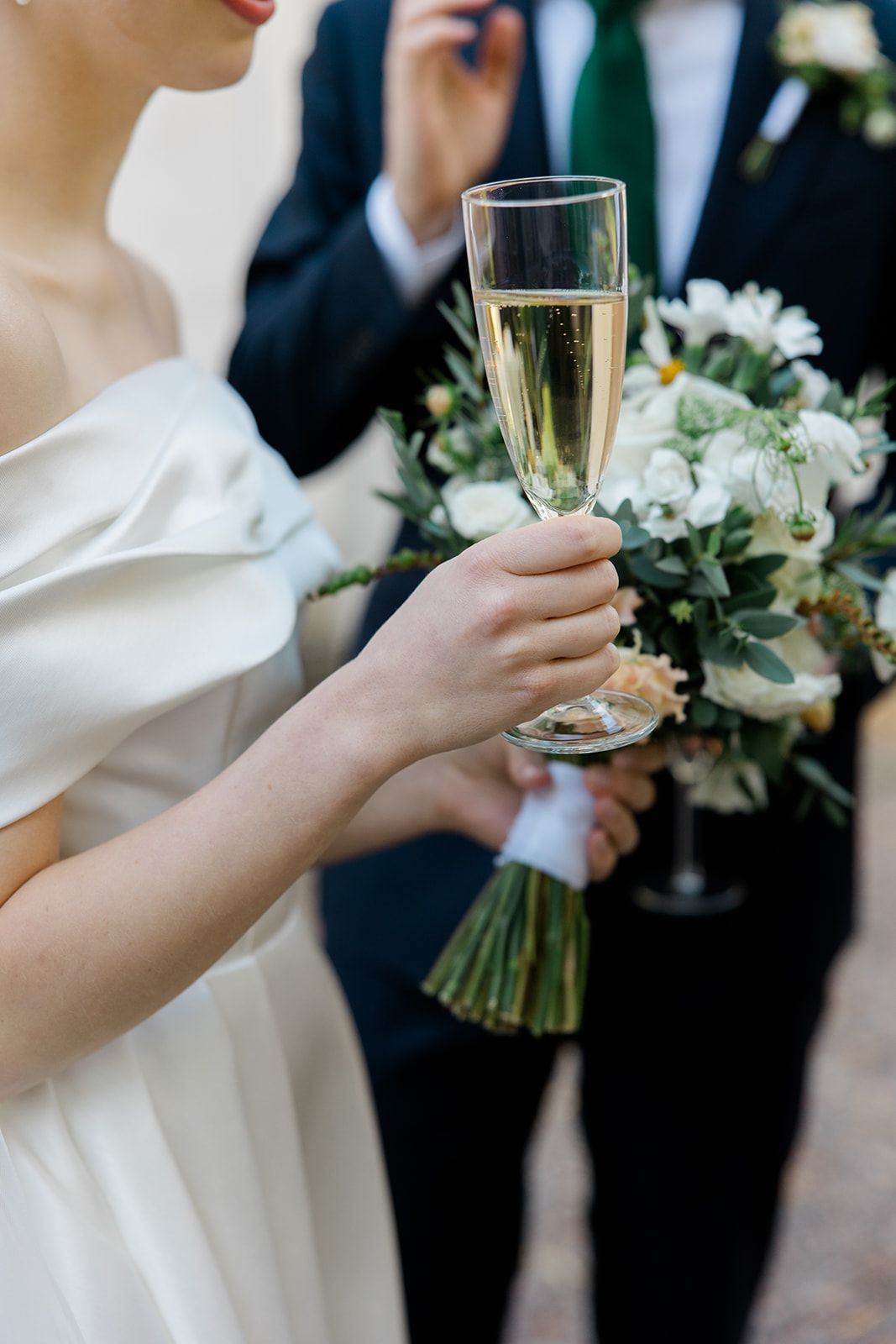 A row of wedding party members holding champagne glasses and white floral bouquets at an elegant celebration.