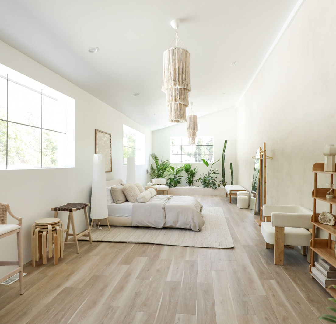 Modern minimalist living room with light wood floors, white walls, and natural lighting through large windows.