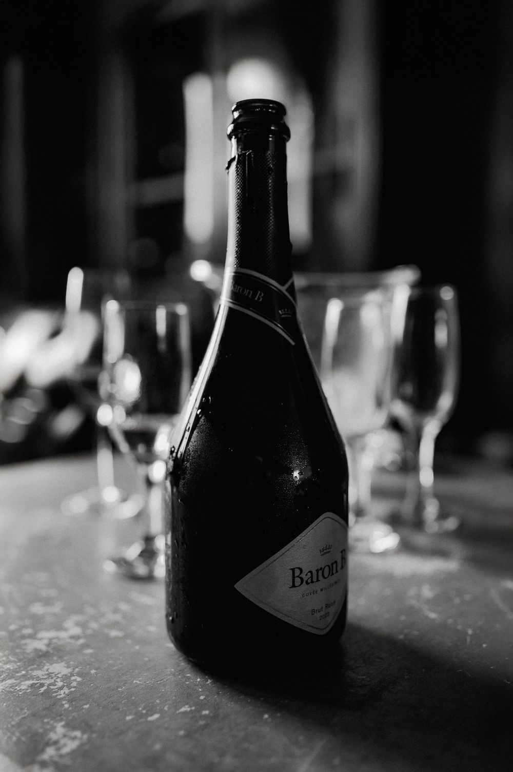 A black and white photograph of a Barefoot wine bottle with wine glasses in soft focus in the background.