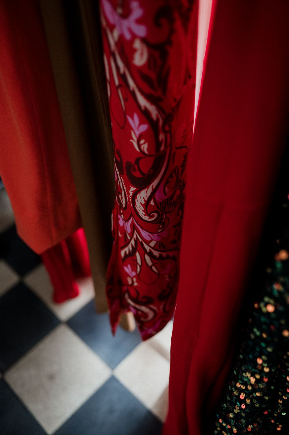 Red curtain with ornate floral pattern drapes elegantly against a checkered floor in dramatic lighting.