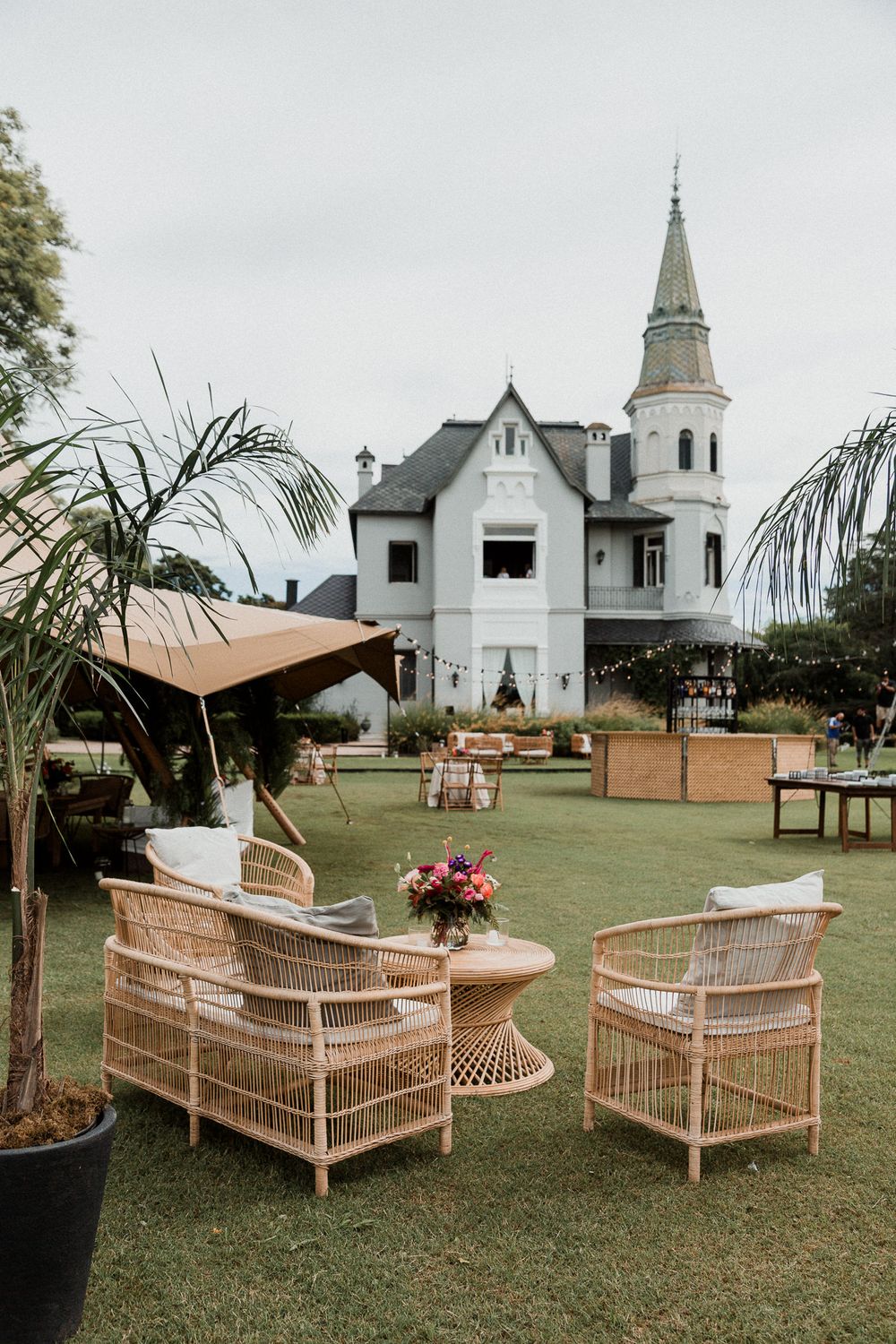 Elegant outdoor wedding venue with rattan furniture and a white church steeple in the background on a cloudy day.