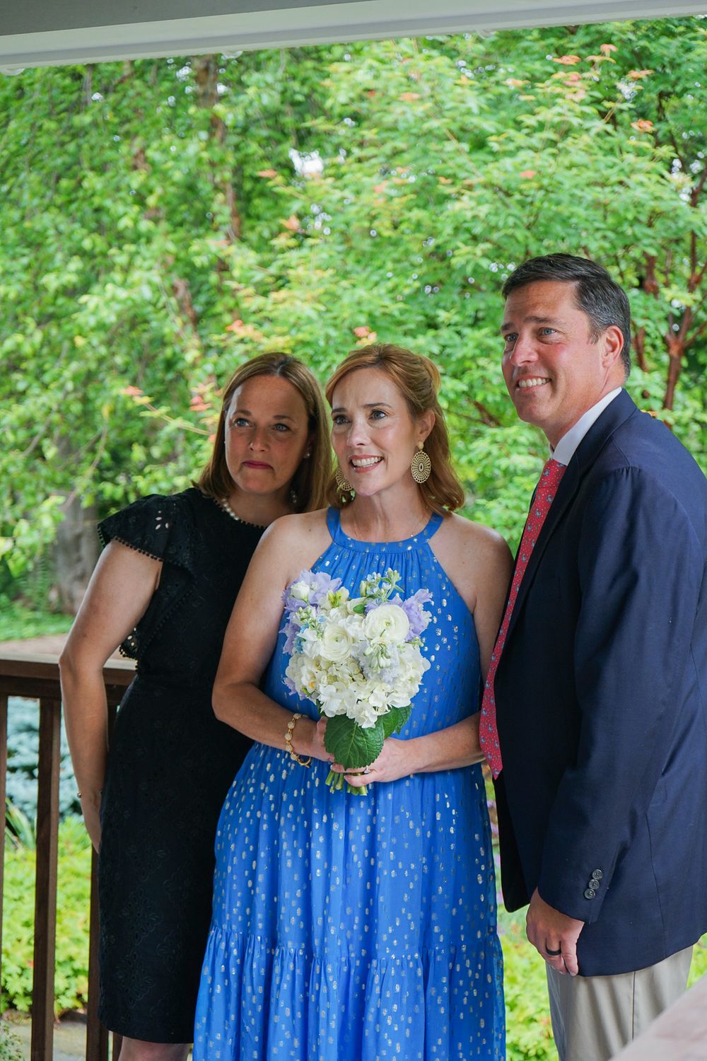 A group of people share joyful moments in a garden setting wearing formal attire including a bright blue dress.