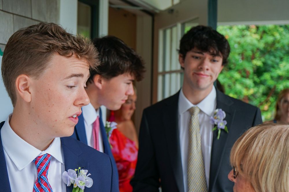 A group of formally dressed people gather at an outdoor event with floral decorations visible in the background.