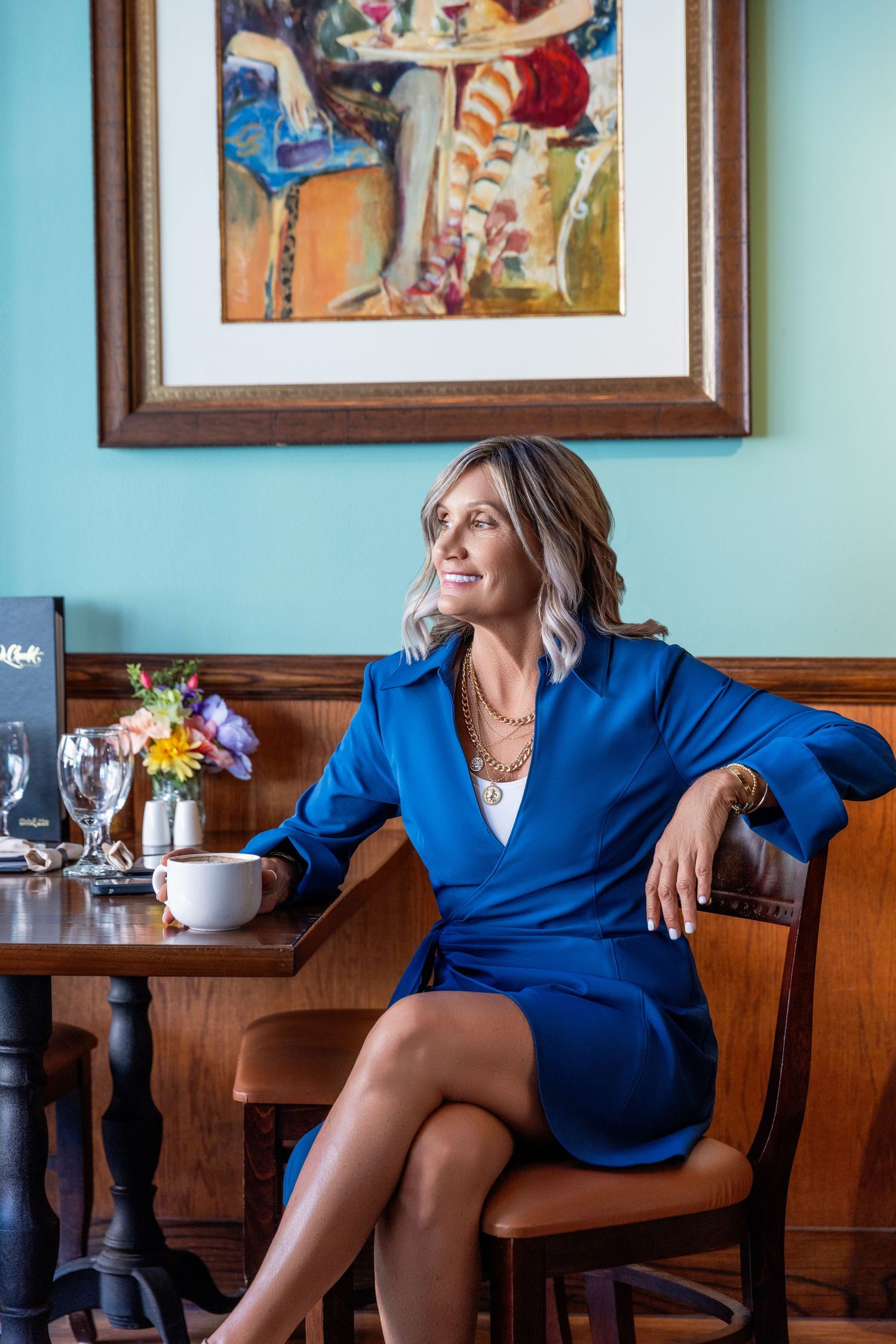 Person in bright blue dress shirt sits at restaurant booth with turquoise walls and framed artwork in background.