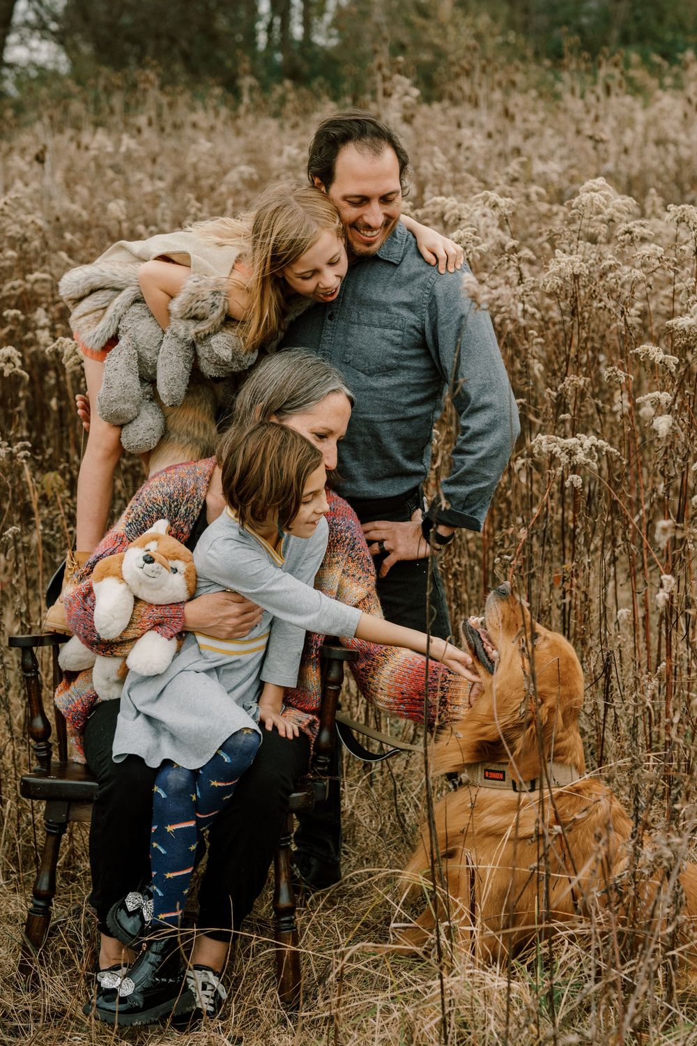 Family shares tender moments together in a rustic autumn field setting.