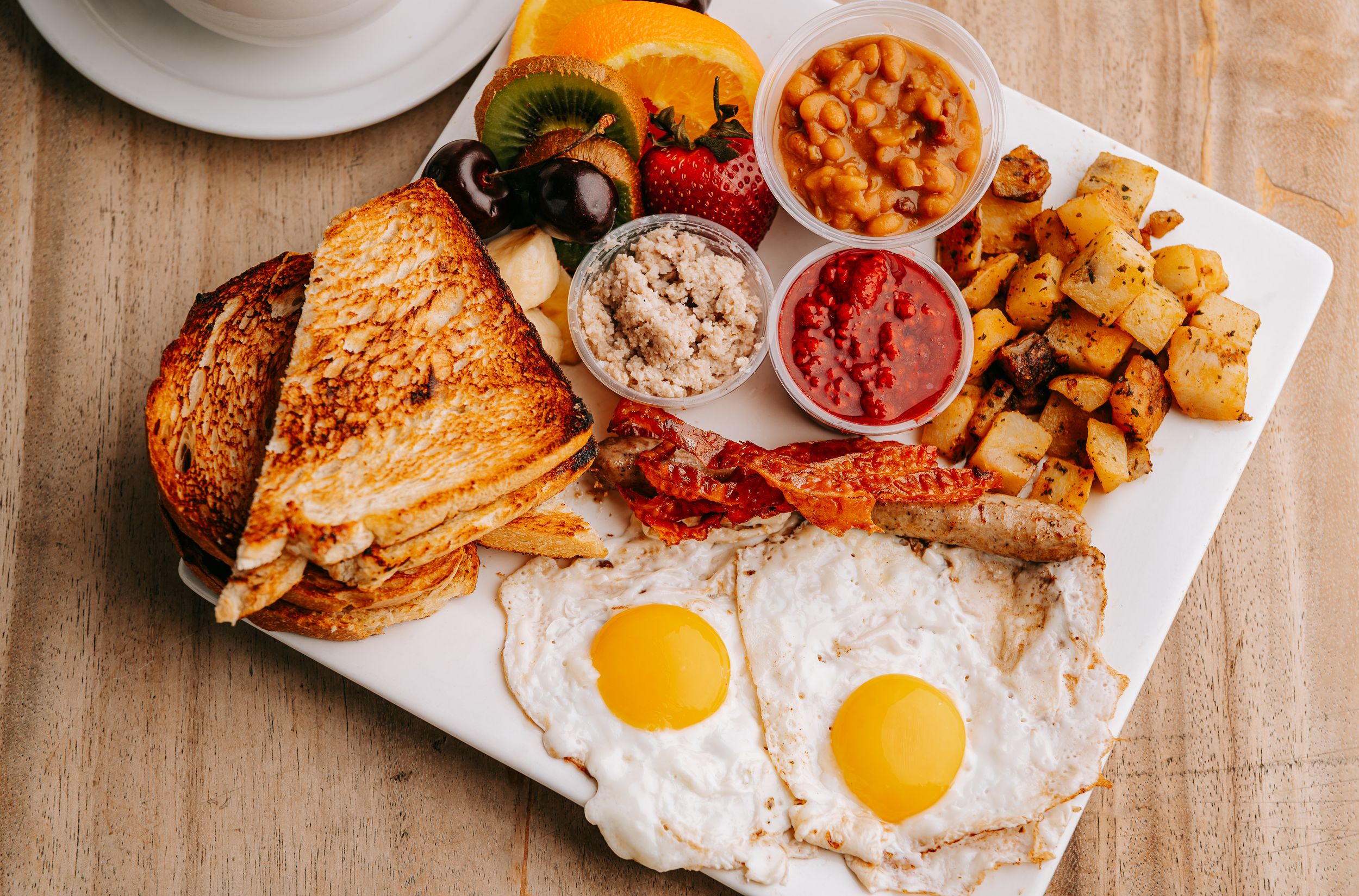 Breakfast plate with sunny side up eggs, toast, potatoes and various sides on wooden table.