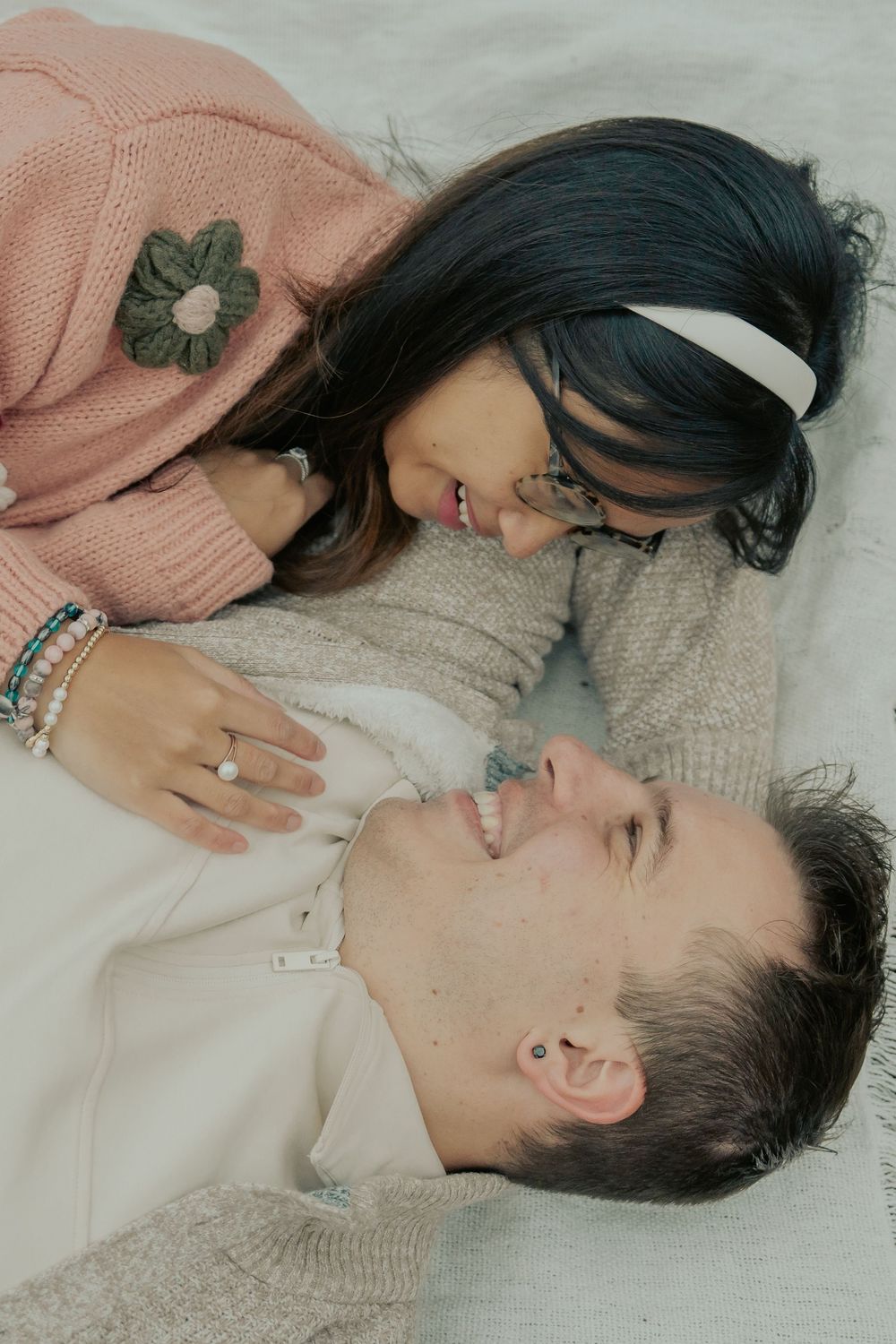 A series of intimate artistic portraits showing two people lying down together in soft pink and gray tones.