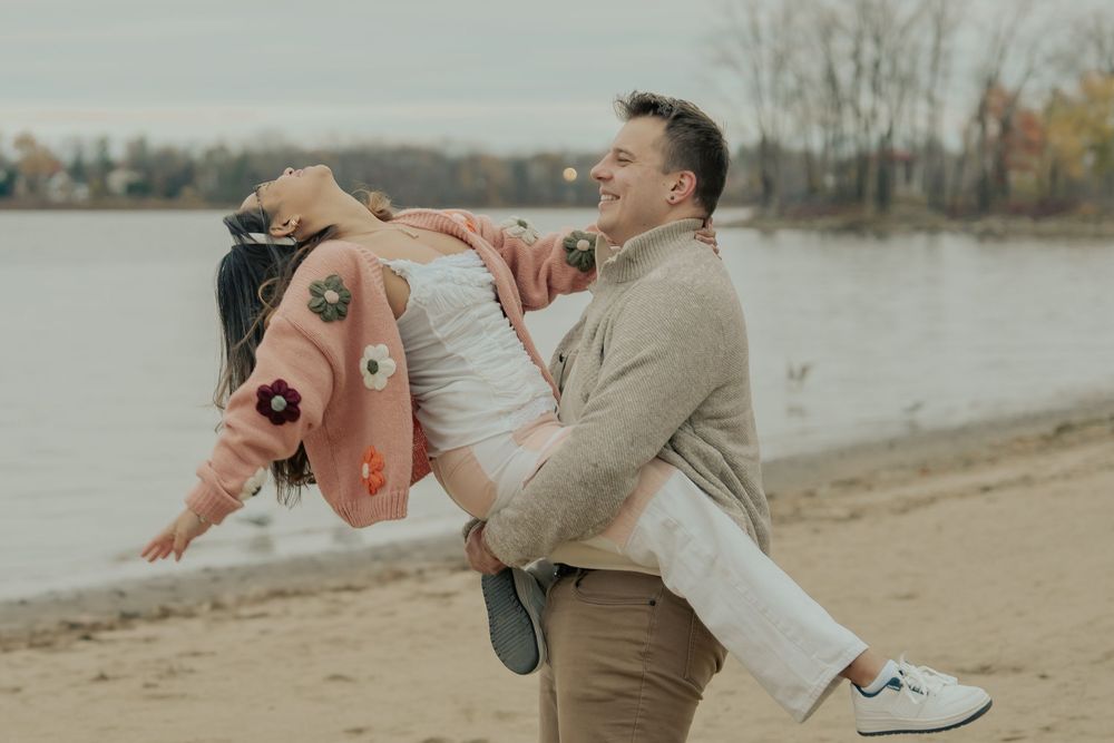 A couple in casual attire shares a romantic moment while dancing together on a beach at sunset.