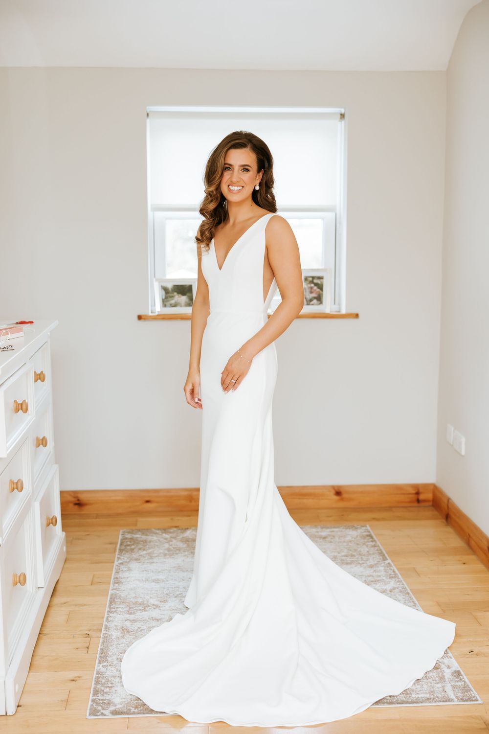 Elegant white wedding dress with flowing train displayed in a minimalist room with hardwood floors. Castle Leslie