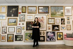 A gallery wall displays numerous framed artworks and photographs in a white-walled exhibition space.