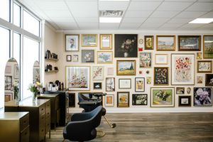 Art gallery interior with framed artwork displayed on white walls and black leather seating in the viewing area.