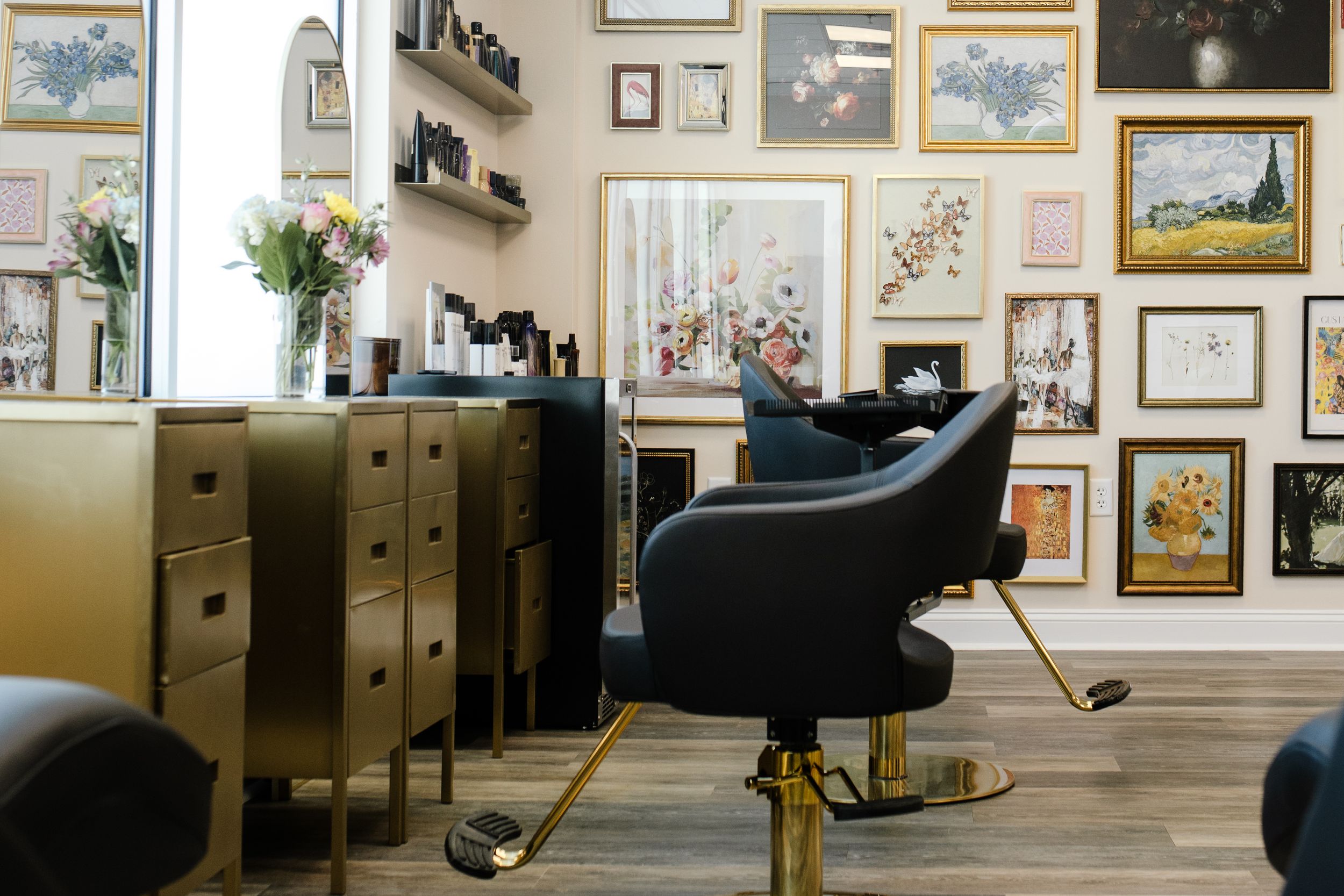 Interior of a stylish salon with black leather chairs, gold filing cabinets and a gallery wall of framed artwork.