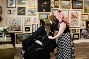 People interact in an art gallery with framed artwork covering the walls in a salon-style display.