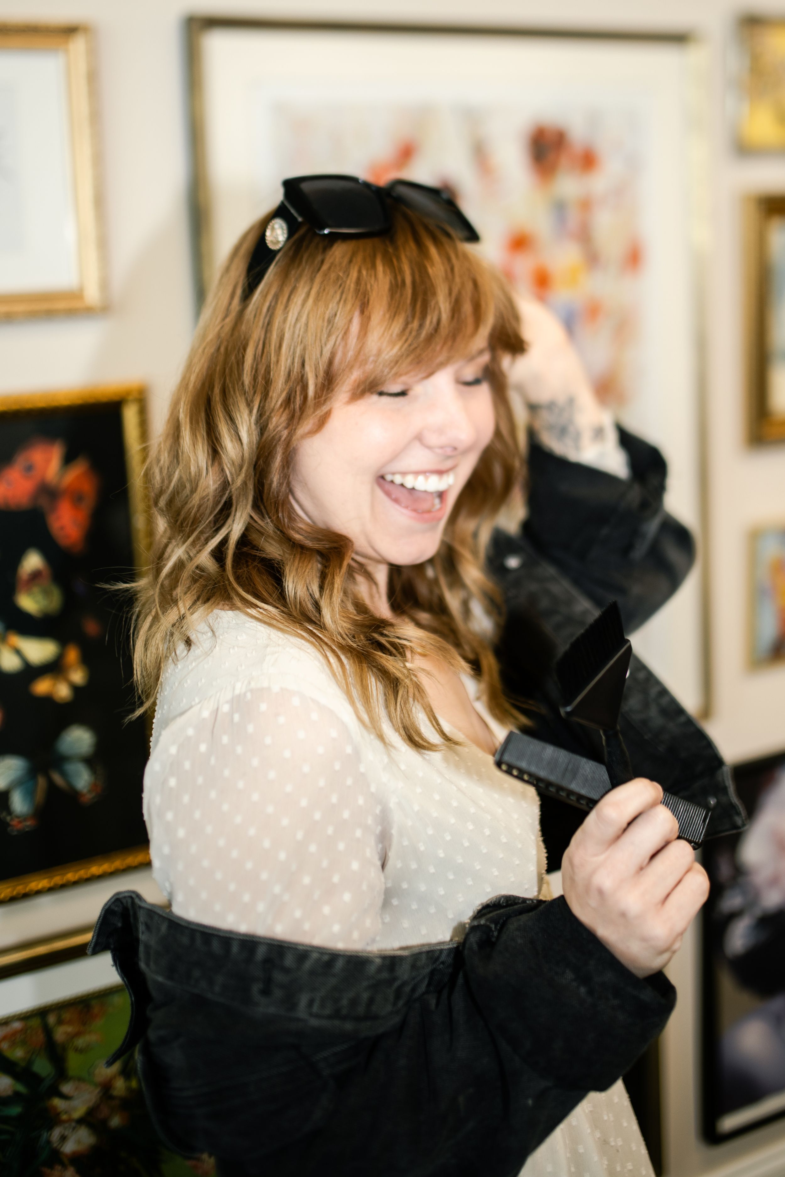A joyful moment captured showing someone laughing while wearing a white polka dot dress and black jacket in an art gallery.