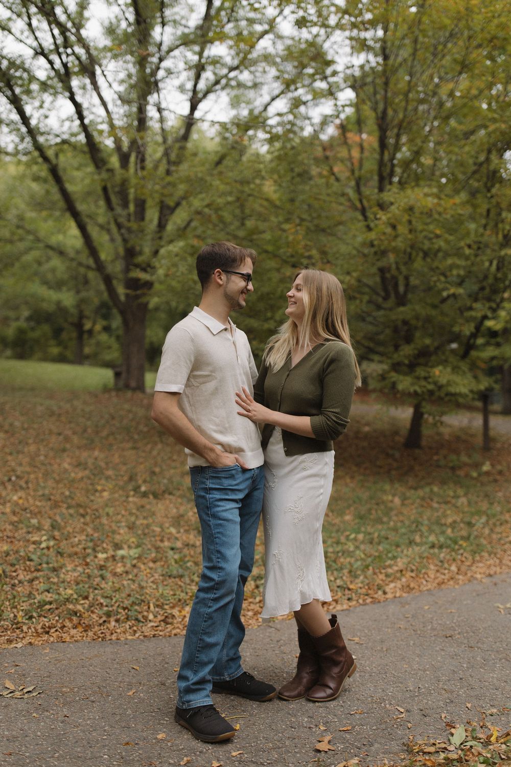 A couple shares a romantic moment on a leaf-covered path in an autumn park.