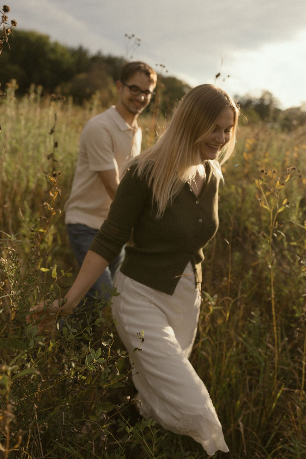 A romantic couple walks through tall grass and wildflowers in a dreamy autumn field.