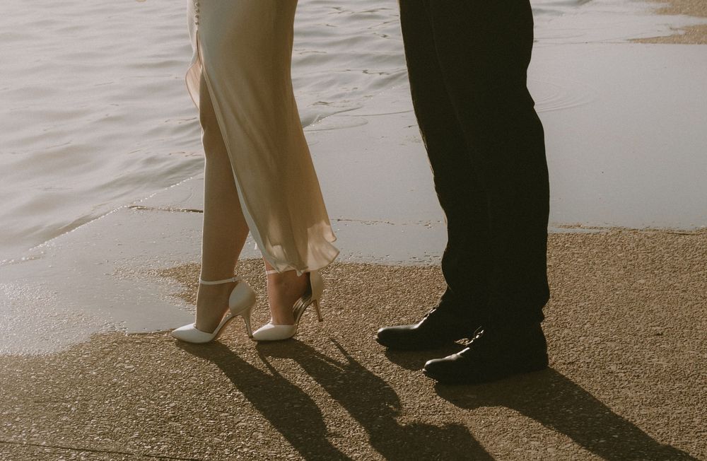 Cropped view of couple's feet walking on sandy beach at sunset with soft waves in the background.