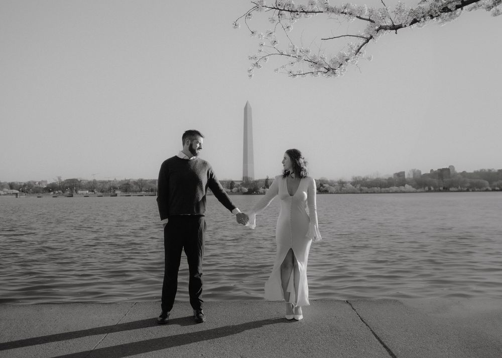 Black and white photo of couple standing by water with Washington Monument in distance.