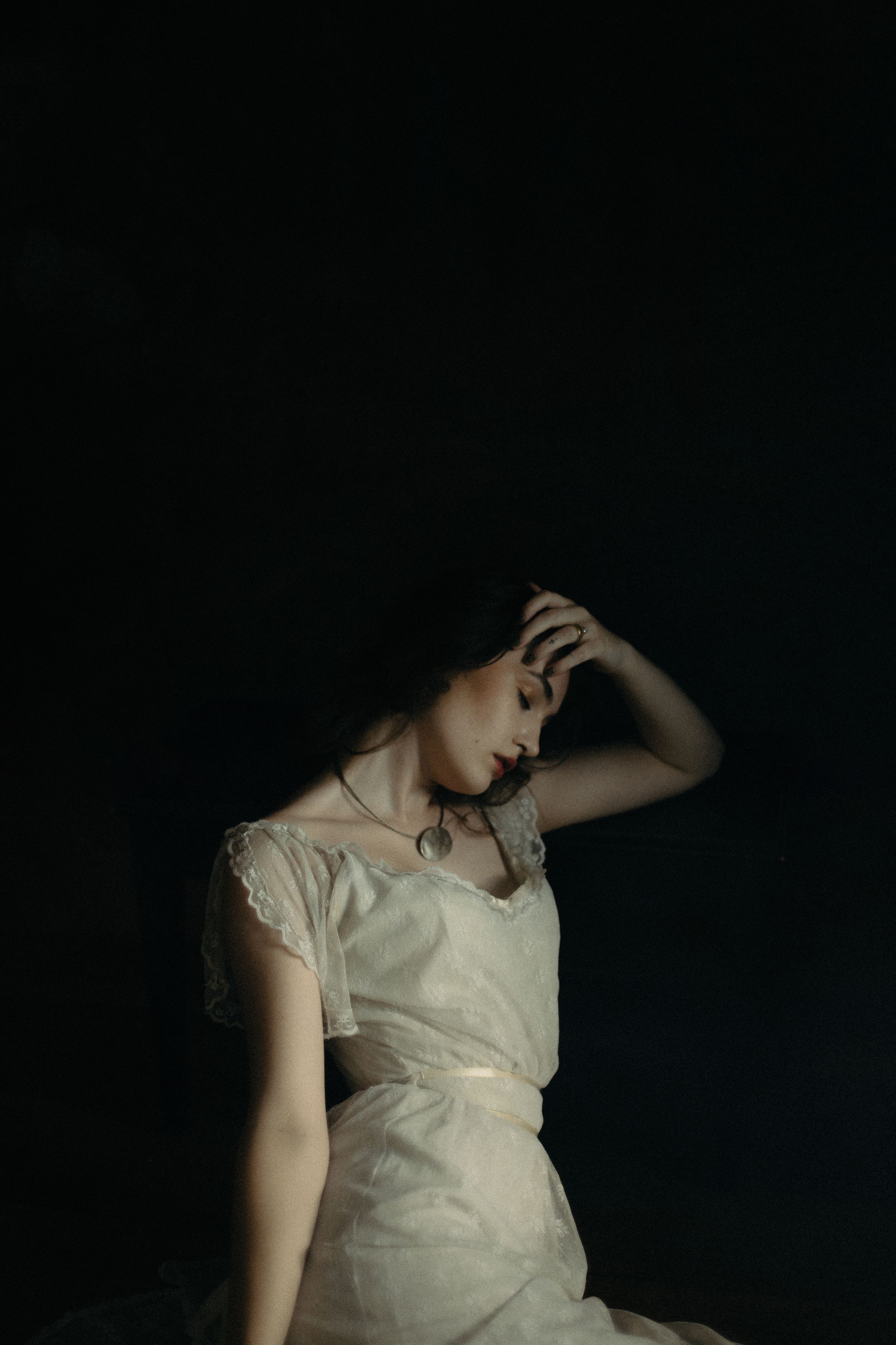 A person in a white dress poses dramatically against a dark background in a moody artistic portrait.